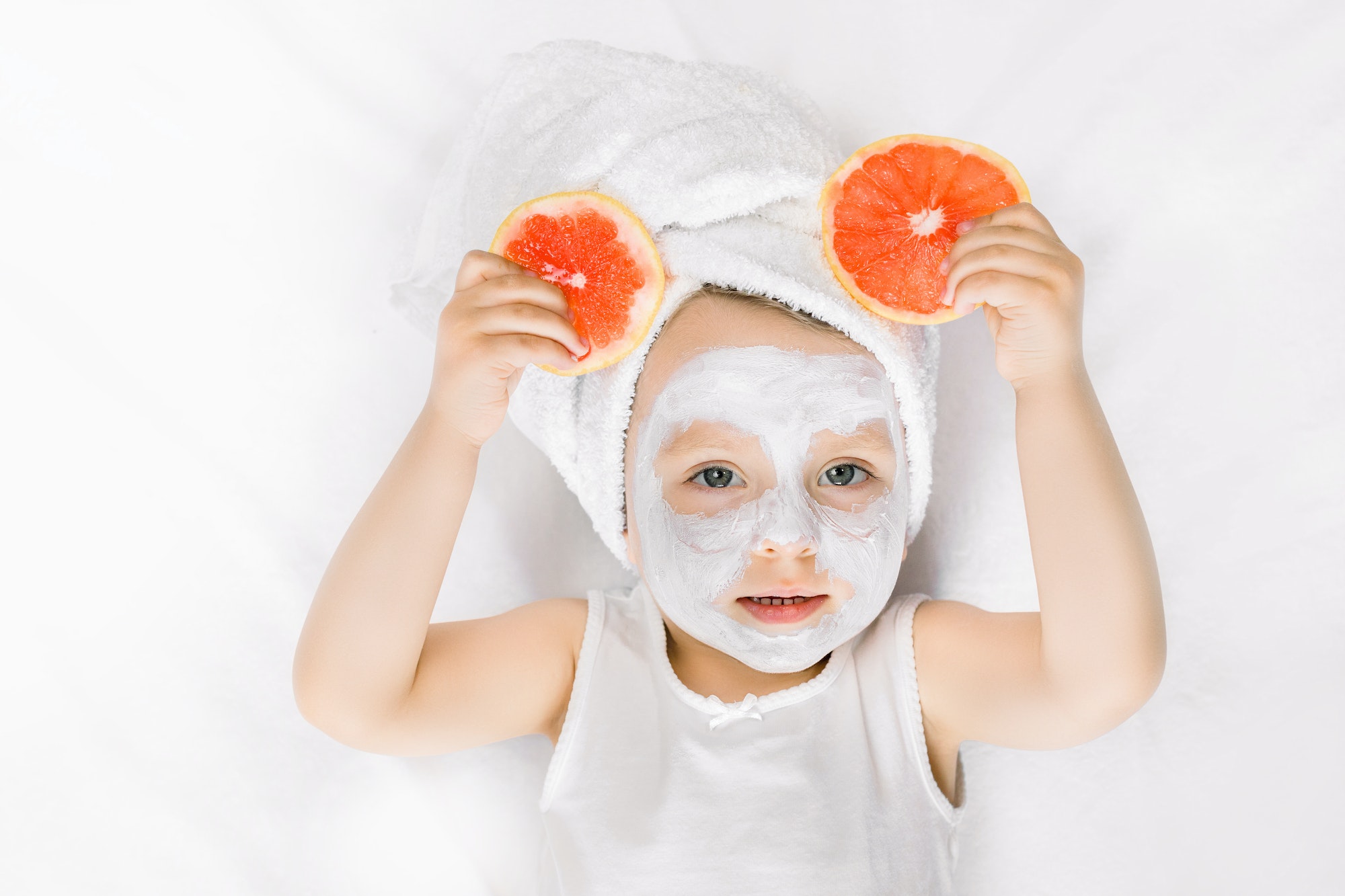 Beauty, spa, hygiene concept for children. Cute little girl with towel on the head, white clay mask